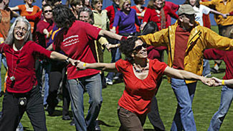 Ljudje se pred dalajlamo držijo za roke in plešejo na športnem stadionu v Seattl