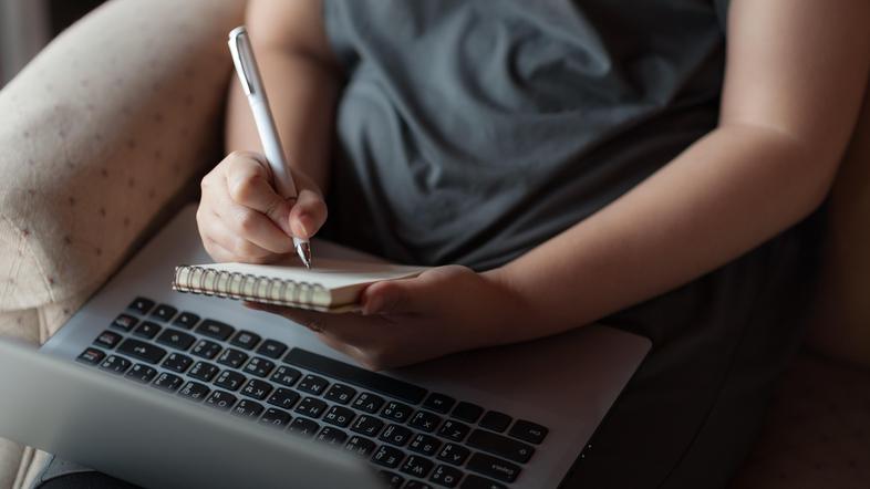 Ženska dela na računalniku in zraven piše v beležnico