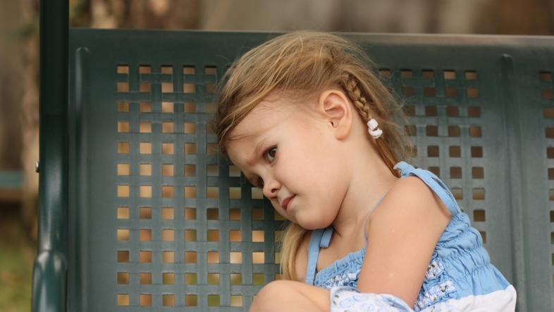 žalostna deklica sedi na klopci