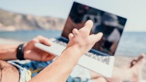 Moški z računalnikom na plaži v kopalkah