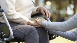 strarejša ženska na invalidskem vozičku, mlajša jo drži za roko