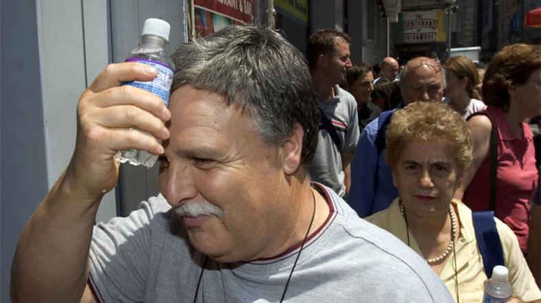 Moški v New Yorku se hladi s steklenico mrzle vode na čelu.