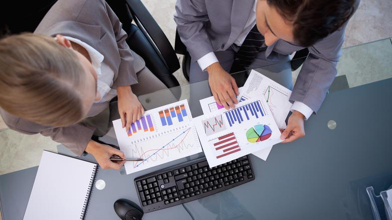 Pisarniški delavci sedijo ob mizi in gledajo grafe