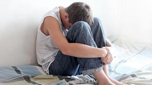 Fant na postelji objema kolena in joka