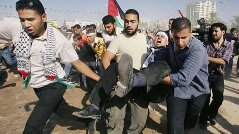 Udeleženci protesta bežijo z ranjenim Palestincem pred streljanjem policistov.