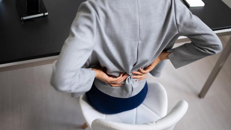 Ženska sedi na stolu in si masira boleč križ