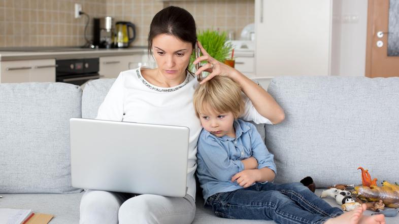 mama telefonira otrok sedi na kavču gledata v prenosni računalnik