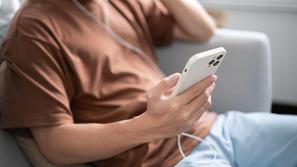 moški drži v roki telefon in posluša glasbo