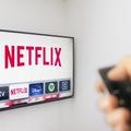 oseba drži daljinca usmerjenega v televizijo na kateri je odprta aplikacija netflix