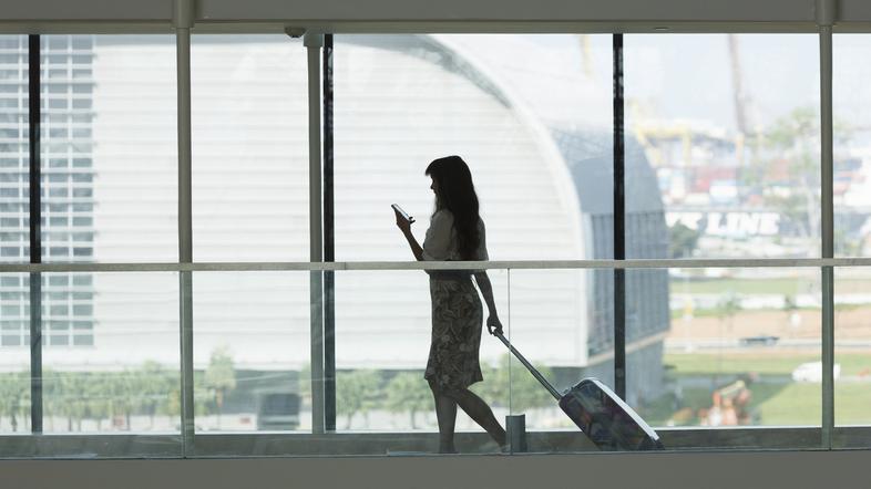 ženska na letališču s kovčkom in telefonom v roki