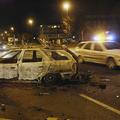 Policijski avtomobil se pelje mimo zažganih ostankov vozila, žrtve nočnega nasil