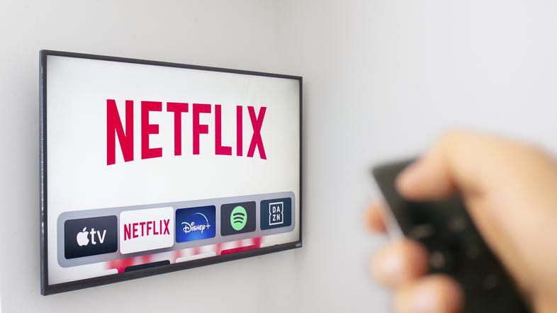 oseba drži daljinca usmerjenega v televizijo na kateri je odprta aplikacija netflix