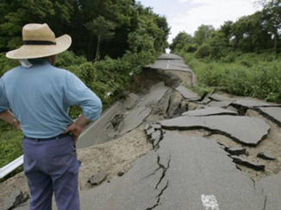 Prebivalec prizadetega območja si ogleduje škodo na cesti, ki jo je povzročil po