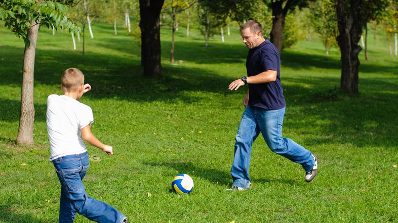 oče in sin igrata nogomet na travi