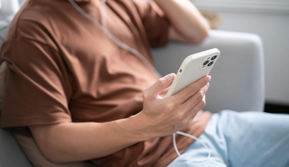 moški drži v roki telefon in posluša glasbo