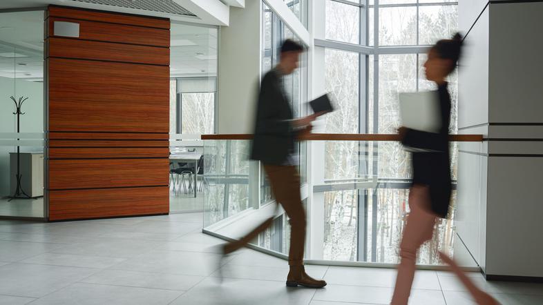 Moški in ženska v obleki hodita po hodniku pisarne