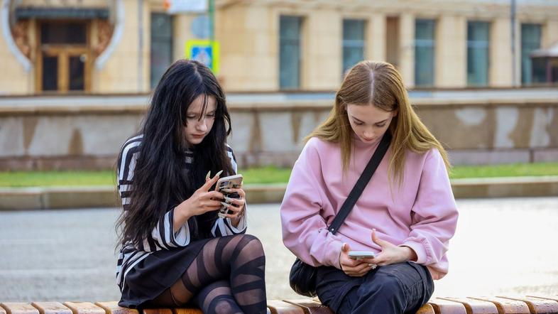 najstnici sedita na klopi v mestu s telefonoma v rokah