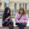 najstnici sedita na klopi v mestu s telefonoma v rokah