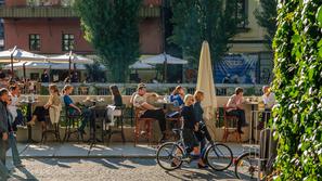 ljudje sedijo v lokalih ob Ljubljanici