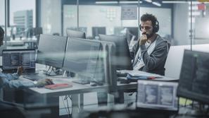 Moški programer v pisarni za računalnikom z zasloni