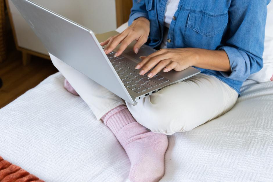 Ženska sedi na postelji z računalnikom v naročju | Avtor: Profimedia