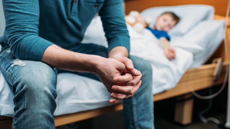 oče sedi na bolniški postelji ob sinu