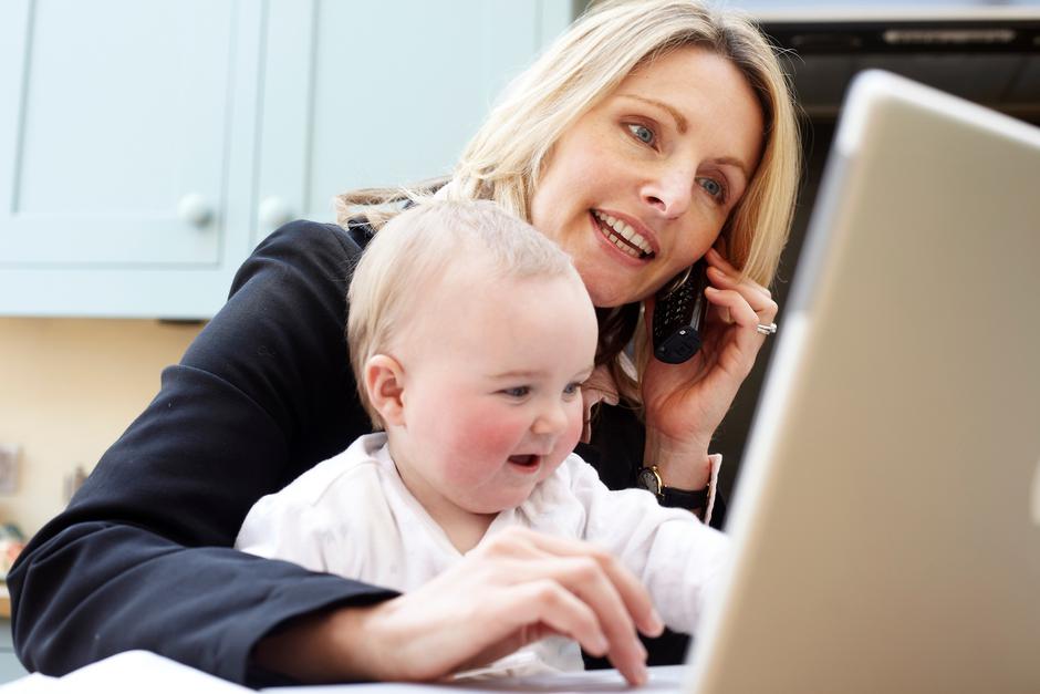 Ženska za računalnikom s telefonom in otrokom v naročju | Avtor: Profimedia