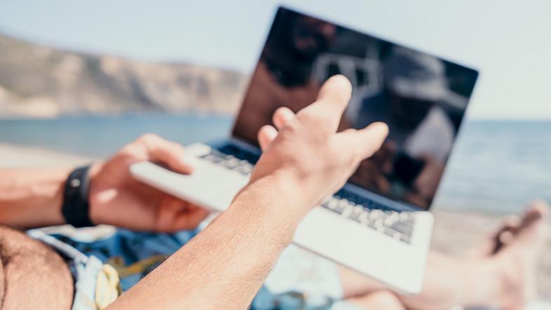 Moški z računalnikom na plaži v kopalkah